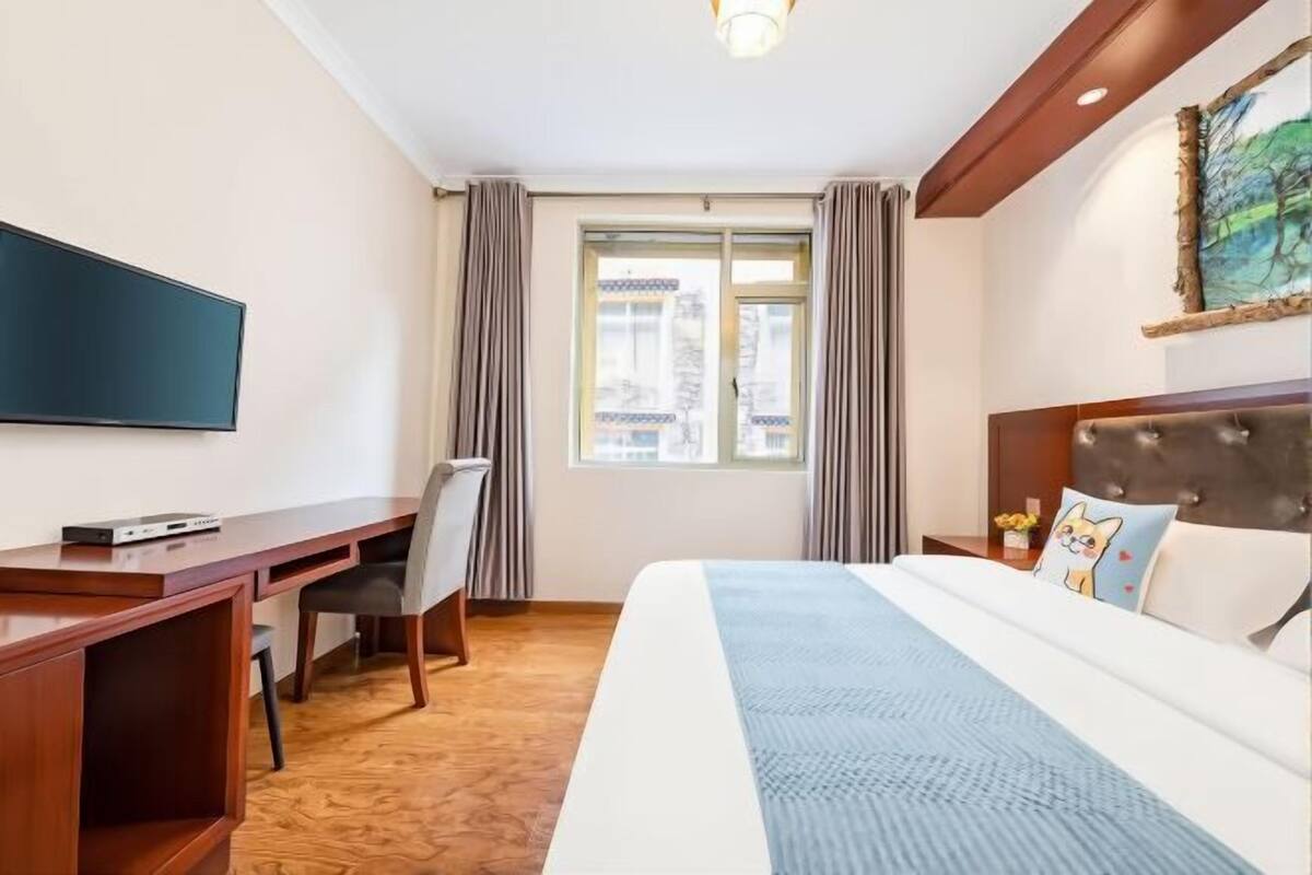 Une chambre d’hôtel avec un lit, un bureau, une chaise, une télévision et une fenêtre avec des rideaux.