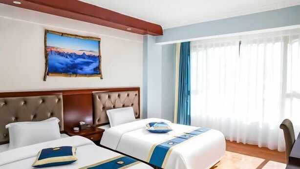 Ein Hotelzimmer mit zwei Betten, einem großen Gemälde an der Wand und Blick ins Freie durch durchscheinende Vorhänge.
