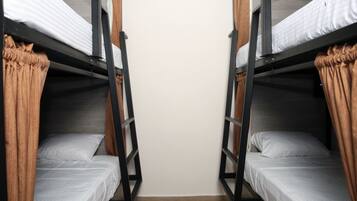 Una habitación con dos literas, cada una con colchón y almohadas, y una cortina a un lado.