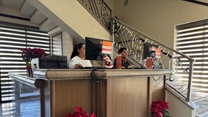 A reception desk with two staff members, a staircase with metal railings, and potted plants. - Hotel Grand Lion (Torreon)