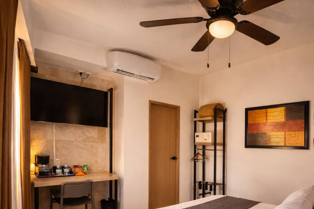 Une chambre à coucher avec un lit, un bureau, une chaise, un ventilateur de plafond et un tableau accroché au mur.