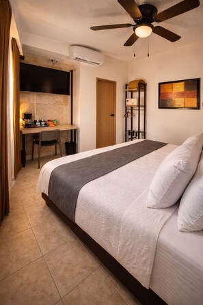 Une chambre à coucher avec un lit, un bureau, une chaise, un ventilateur de plafond et un tableau accroché au mur.