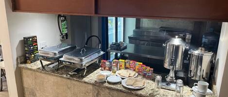 Una barra de desayuno con una máquina de café, un mostrador de comida y un dispensador de agua.