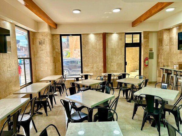 Interior de restaurante con varias mesas y sillas, un ventanal y una puerta.