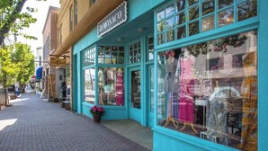 Un hôtel de charme à la façade turquoise, avec de grandes vitrines où sont exposées des robes, et un trottoir pavé de briques.
