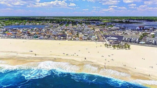 Vue aérienne d’une ville côtière avec une plage de sable, un port de plaisance et des immeubles résidentiels.