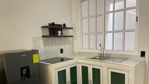 Een kleine keuken met een koelkast, een spoelbak en een raam boven het aanrecht.