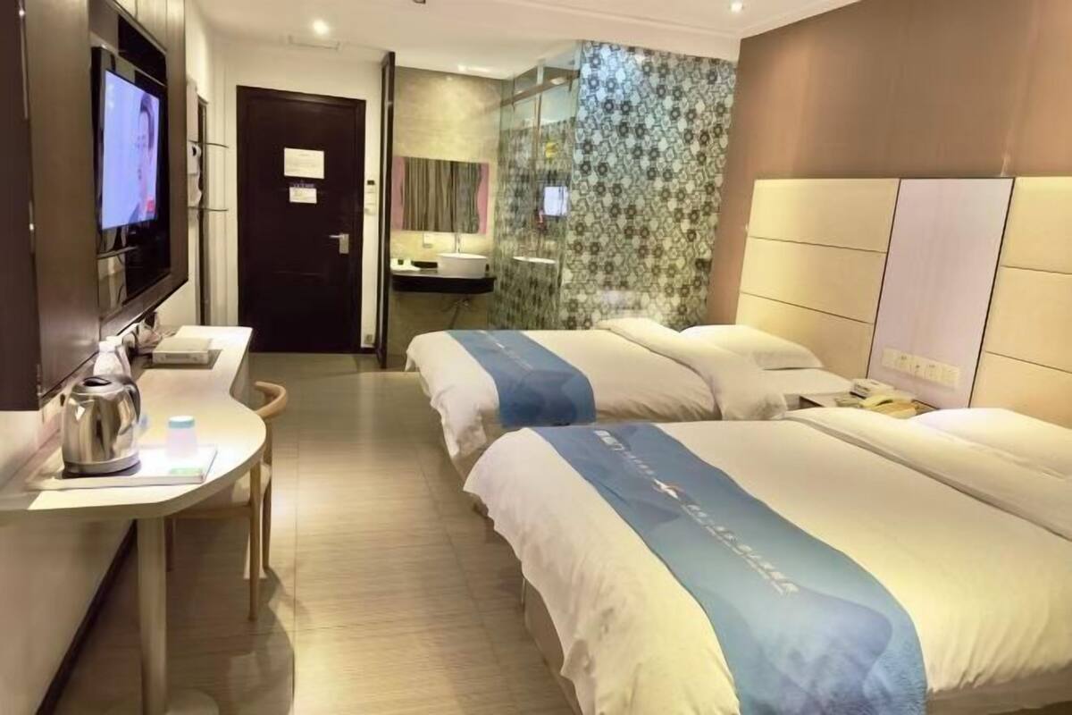 A hotel room with two beds, a TV, a desk with a kettle, and a bathroom with a shower.