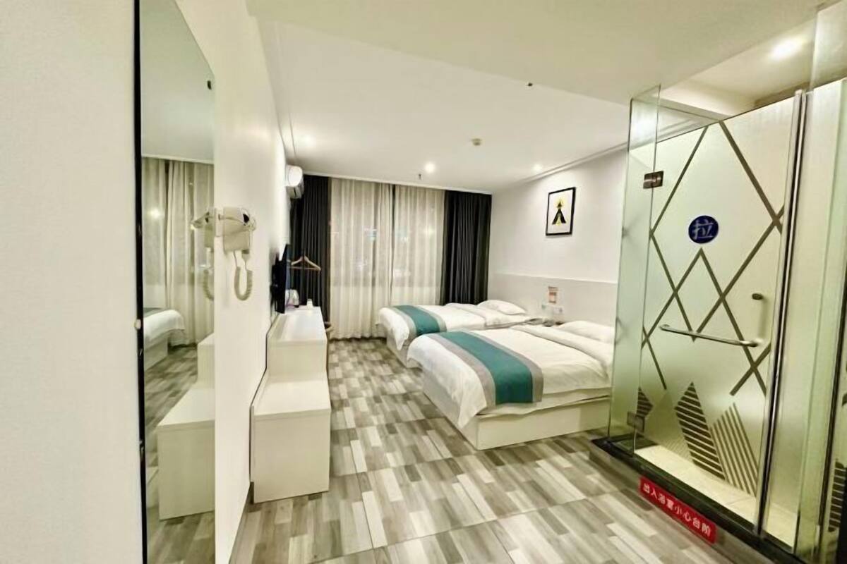 A hotel room with a mirrored wardrobe, a bed with a striped bedspread, a bedside table, and a large mirror.