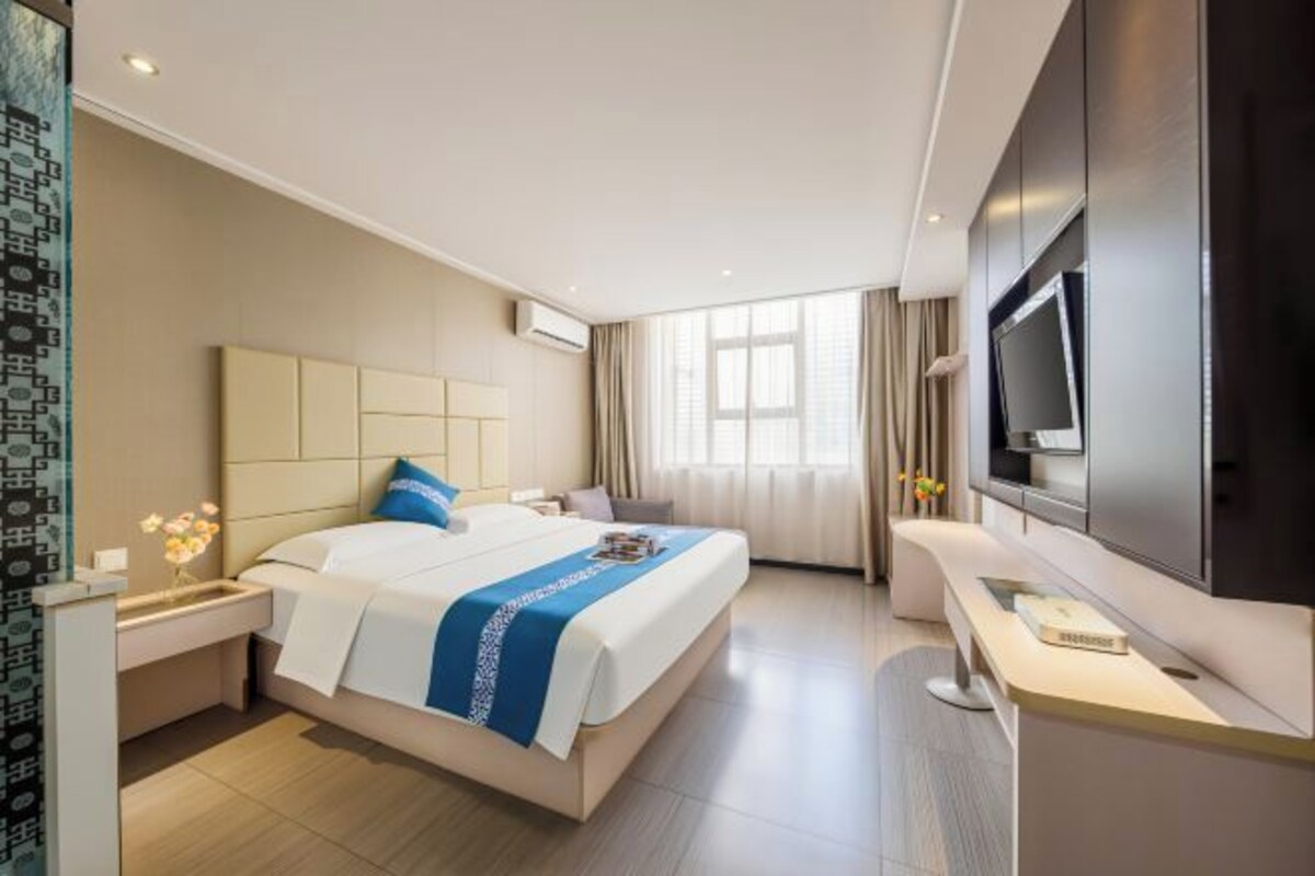 Habitación de hotel con cama, mesita de noche, televisor y un ventanal amplio.