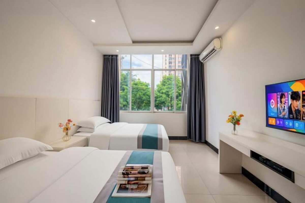 Habitación de hotel con dos camas, un televisor, una ventana con cortinas y un florero con flores.