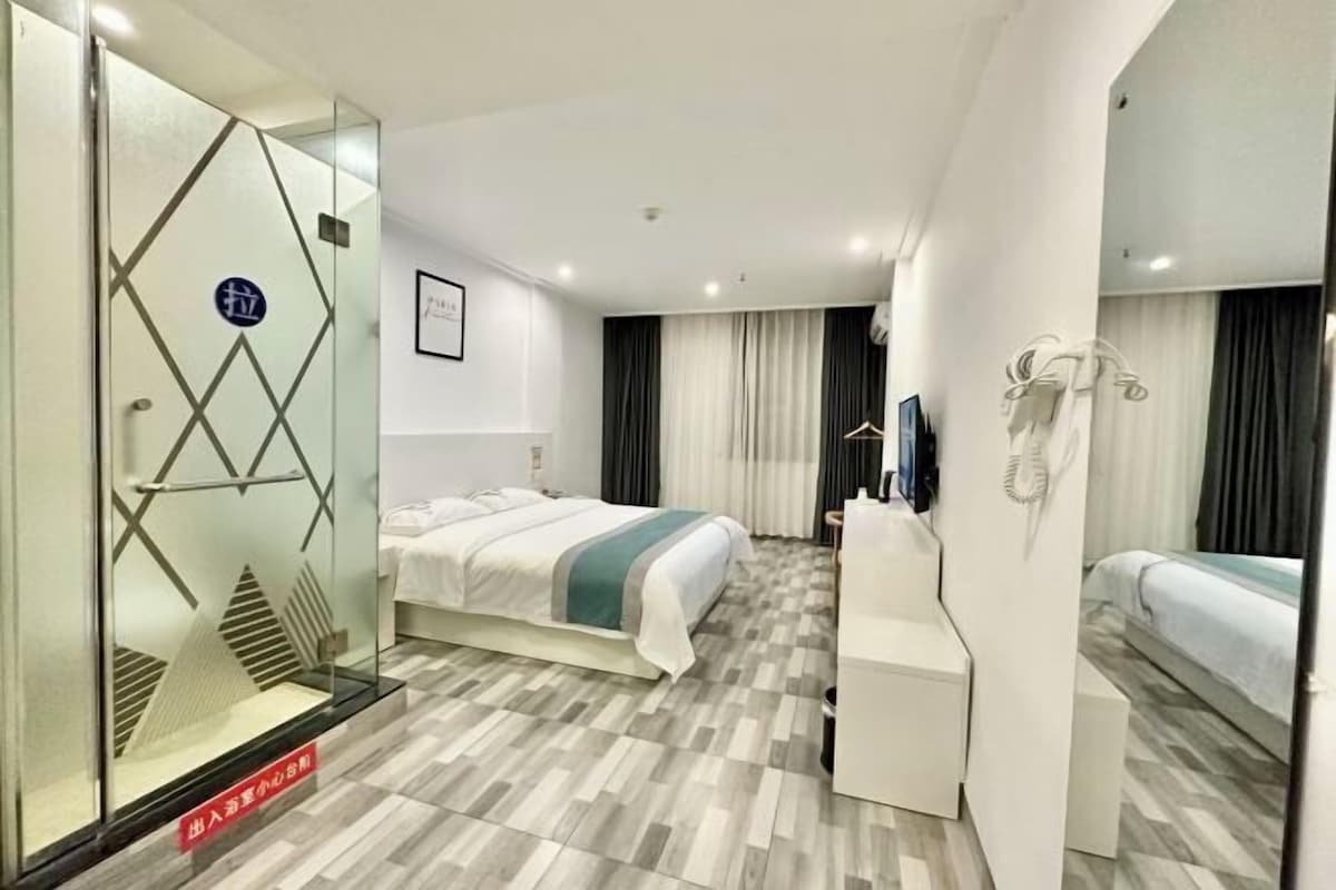 A hotel room with a bed, a desk, a chair, a mirror, and a wardrobe.