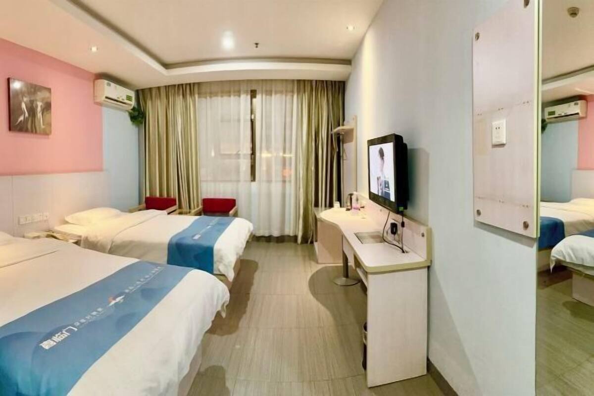 A hotel room with two beds, a desk, a TV, and a large mirror.