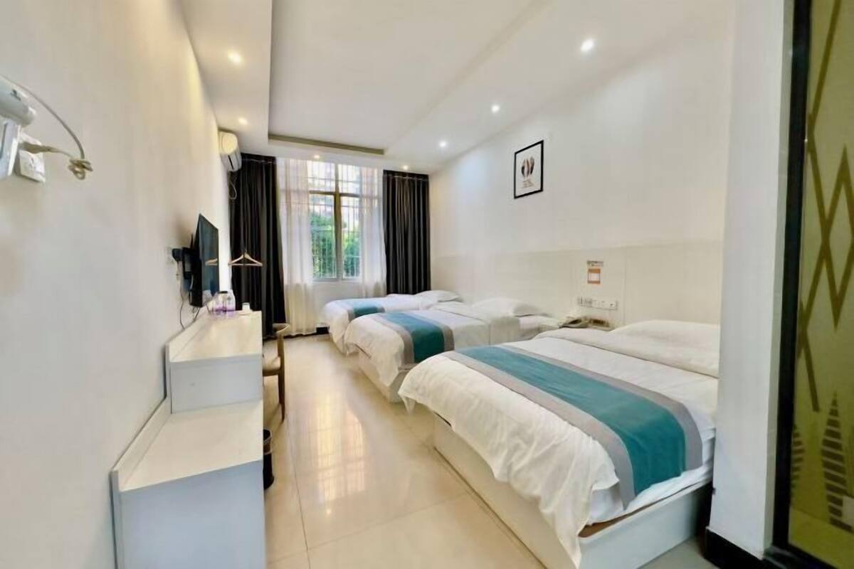 A hotel room with two beds, a desk, a TV, and a window with curtains.