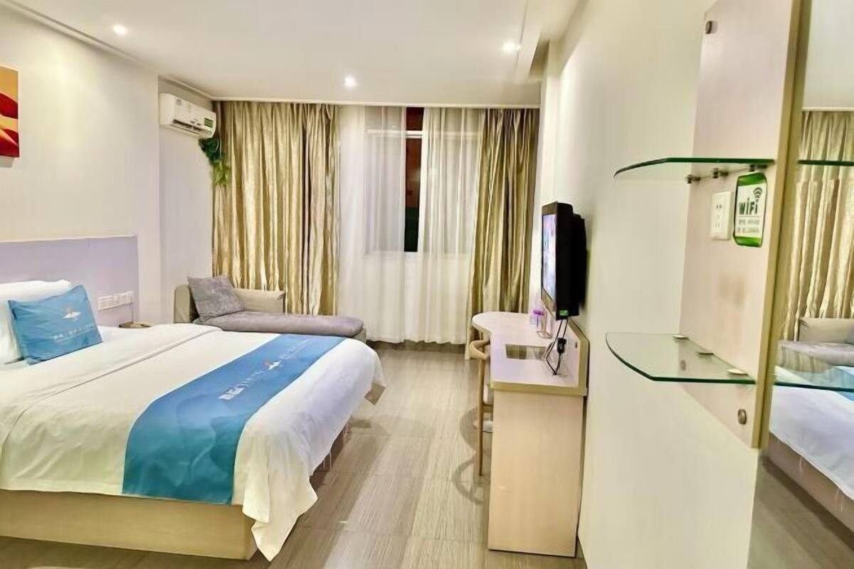 A hotel room with a bed, a desk, a TV, and a window with curtains.