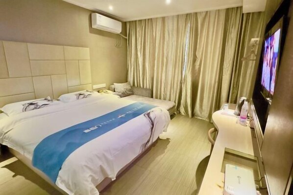 Habitación de hotel con una cama grande, una mesita de noche con televisor y una ventana con cortinas.