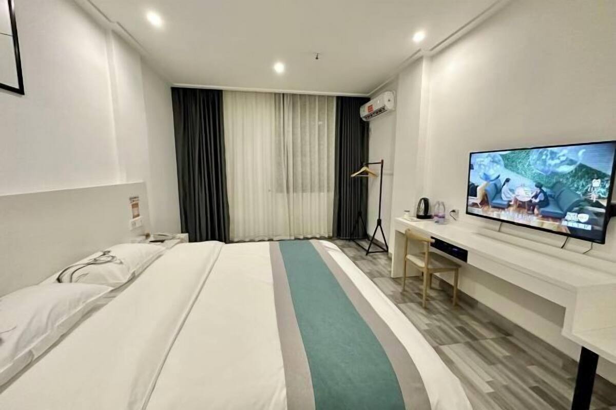 A hotel room with a bed, a desk, a television, and a window with curtains.