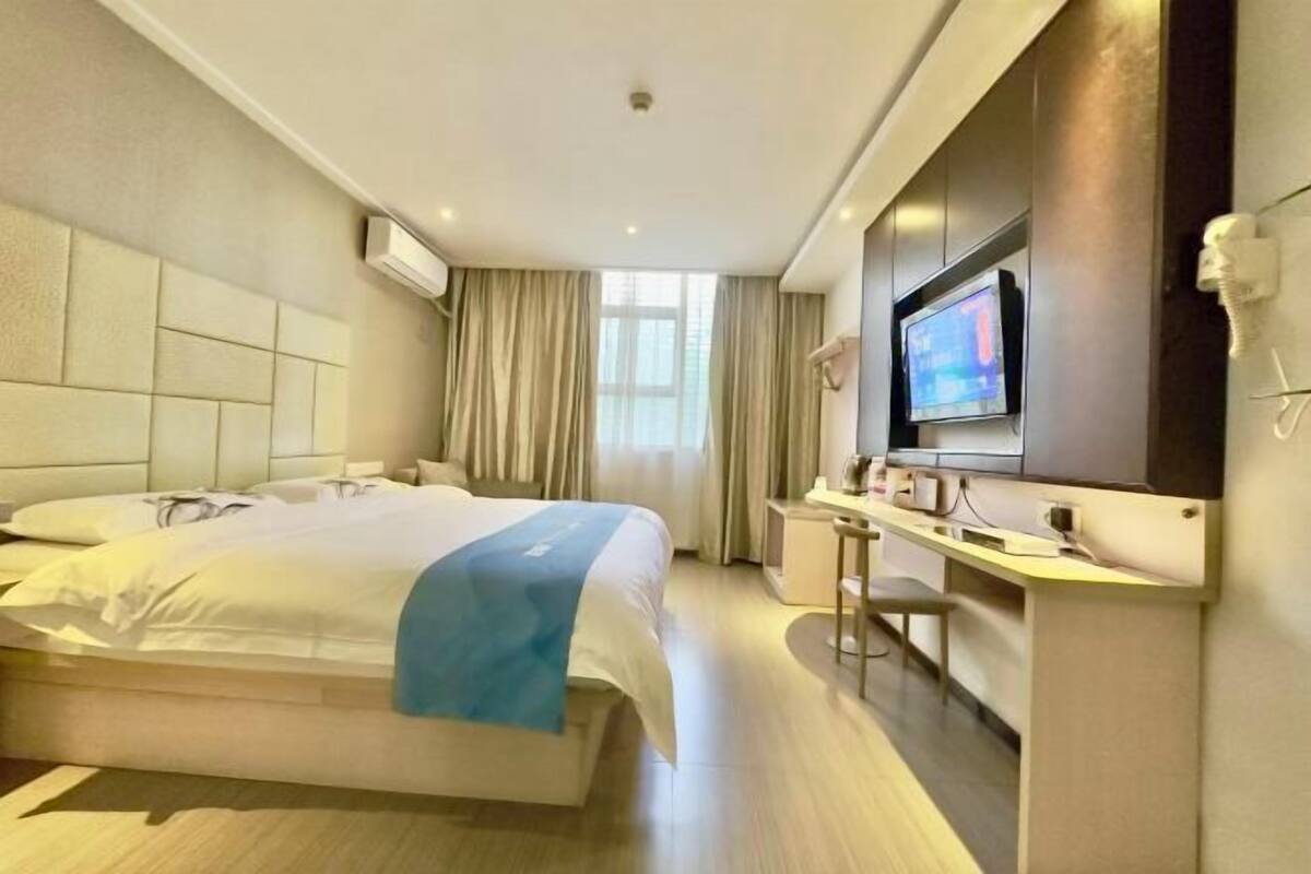 A hotel room with a bed, a desk, a TV, and a window with curtains.