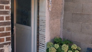 A house entrance with a sliding glass door, a potted plant with hydrangeas, a bench, and a small awning.