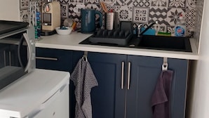 A compact kitchen with a microwave, a kettle, and a sink. The backsplash features a geometric tile pattern.