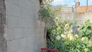 A patio with a red table and chairs, a doormat, and a garden with flowers and a wooden fence.