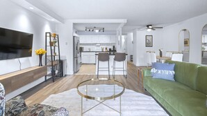 A modern living room with a green sofa, a coffee table, and a TV on the wall. - Stylish Suite at Stampede w/ Free Parking, AC (Calgary)