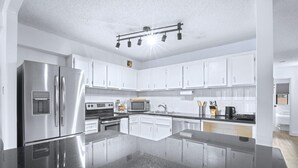 A modern kitchen with white cabinets, stainless steel appliances, a central island, and a black countertop. - Stylish Suite at Stampede w/ Free Parking, AC (Calgary)