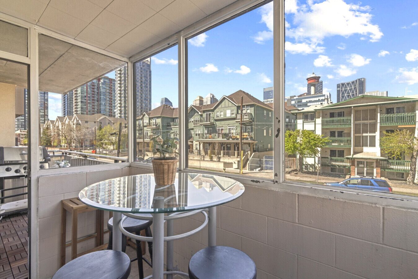 Un balcón con una mesa y sillas de vidrio, con vistas a una zona residencial con varios edificios.