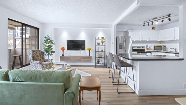 A modern living room with a sofa, a coffee table, and a TV. There is a kitchen with a fridge, microwave, and bar stools. - Stylish Suite at Stampede w/ Free Parking, AC (Calgary)