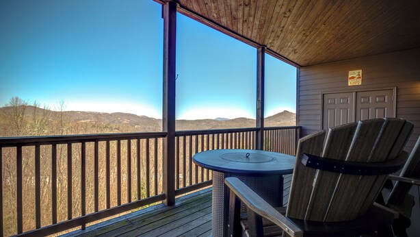 Une terrasse en bois avec une table et des chaises, offrant une vue sur un paysage montagneux.