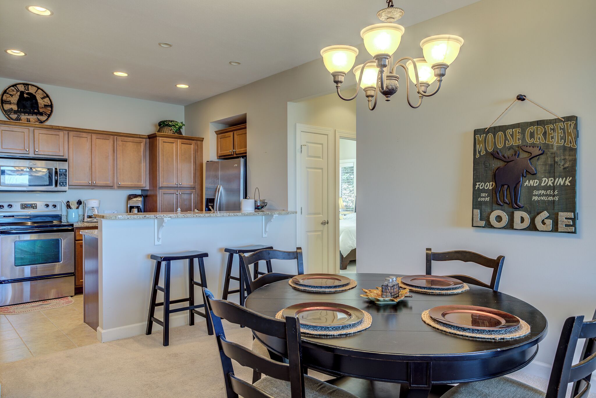 A modern kitchen with a central island, wooden cabinets, stainless steel appliances, and a dining area with a round table and chairs.
