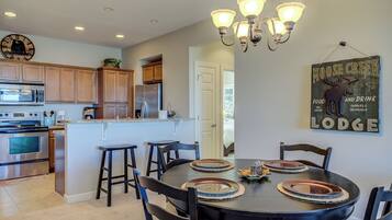 A modern kitchen with a central island, wooden cabinets, stainless steel appliances, and a dining area with a round table and chairs.