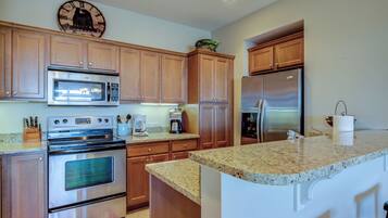 A kitchen with wooden cabinets, stainless steel appliances, a granite countertop, and a wall clock.