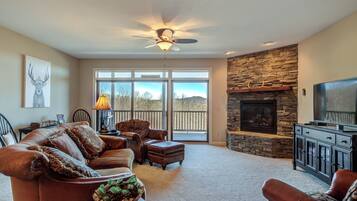 A spacious living room with a leather sofa, a fireplace, a television, and a ceiling fan.