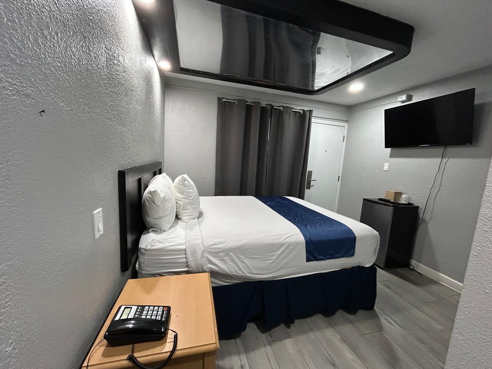 Ein Hotelzimmer mit einem Bett, einem Schreibtisch mit Telefon, einem Fernseher und einem Fenster mit Vorhängen.