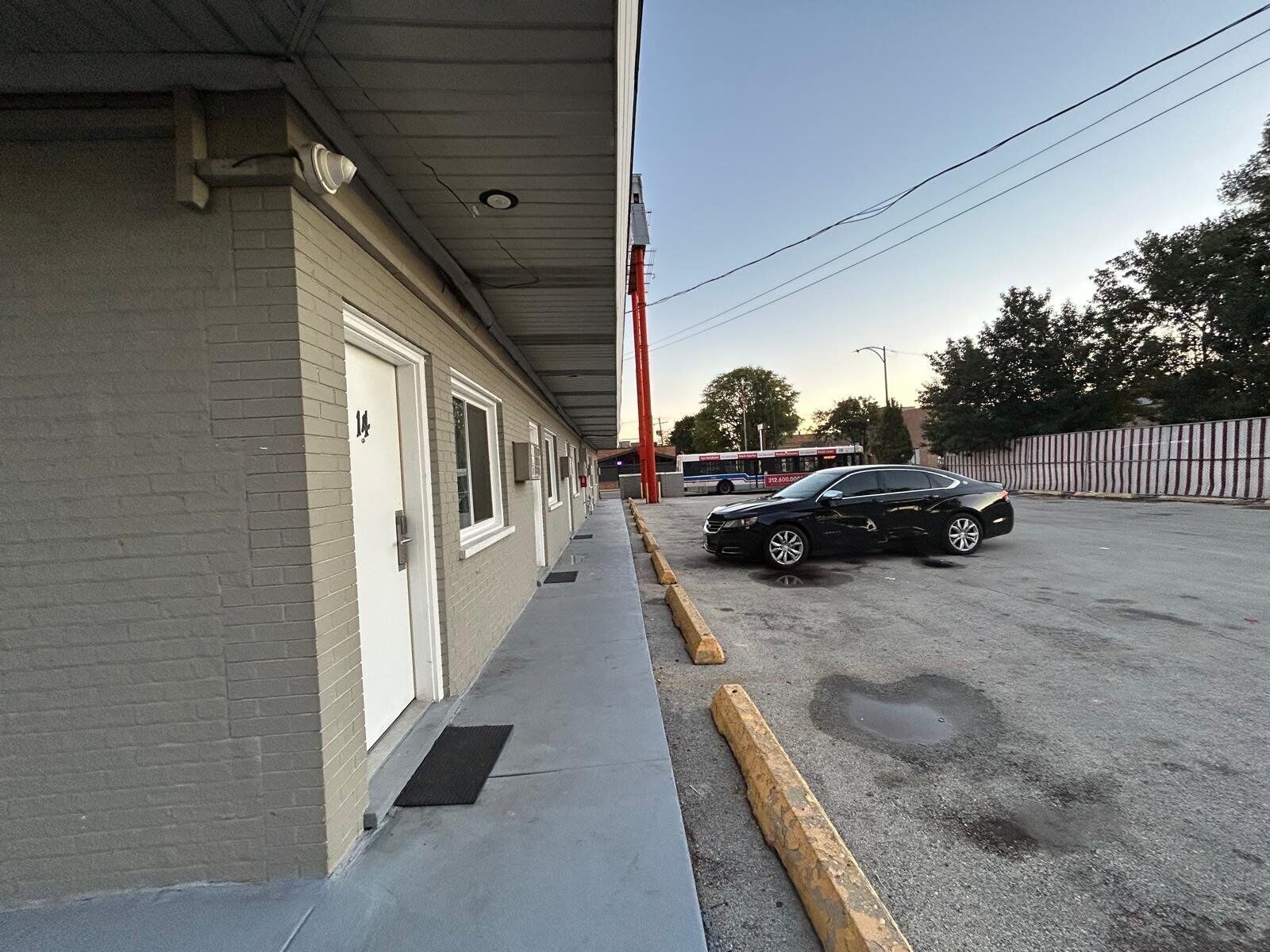 A building with a covered walkway, a parked car, and a bus in the background.