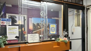 Un comptoir d’accueil avec une cloison en verre, un panneau indiquant qu’il est interdit d’amener des animaux, un autre panneau interdisant de fumer, un code QR pour l’enregistrement et un panneau indiquant un temps d’attente d’une minute pour les clients.