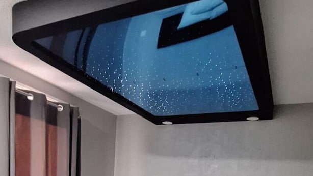 Une chambre d’hôtel moderne dotée d’un grand lit, d’un téléviseur à écran plat fixé au plafond et d’une table de chevet avec une lampe.