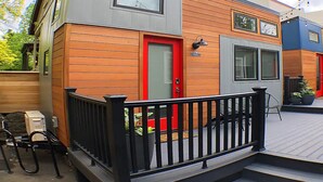 Een tweelaags huis met een rode deur, een zwarte balustrade en een klein terras.