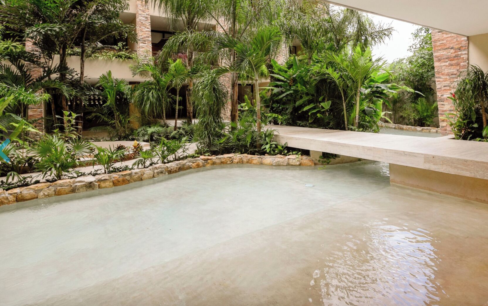 A pool area with a stone border, surrounded by lush greenery and a stone building.