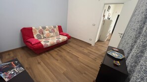 Een kamer met een rode bank, een klein tafeltje met decoratieve borden en een kamerbreed gordijn met dessin.