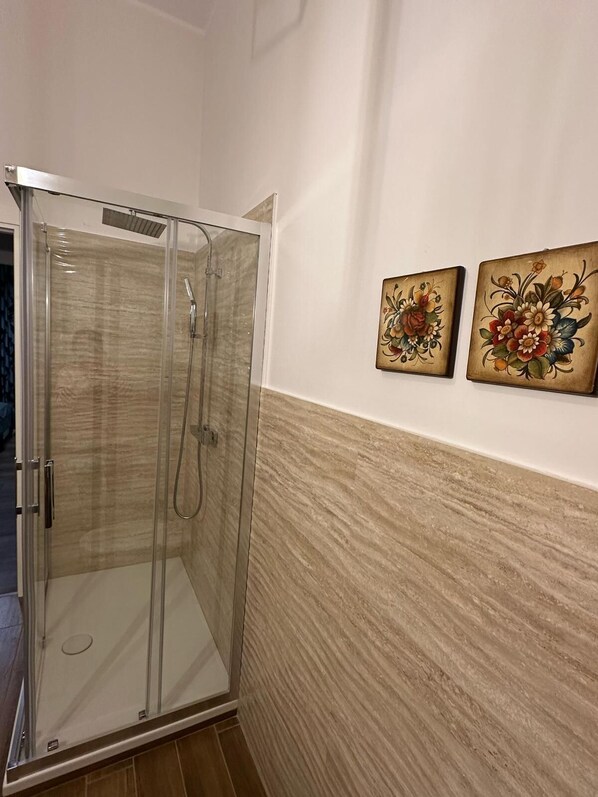 A glass-enclosed shower with a door, a tiled floor, and two floral paintings on the wall. - A walk to the heart of Catania. An apartment with all the amenities. (Catania)