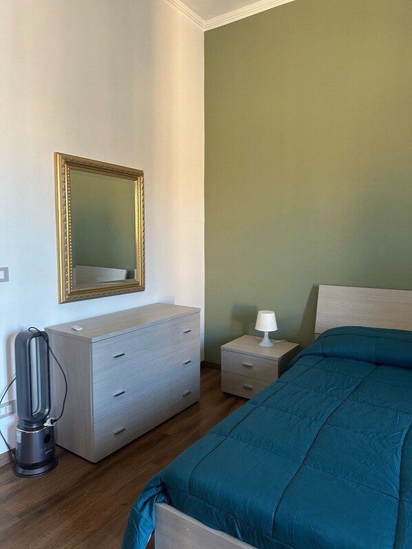 Een slaapkamer met een bed, een dressoir, een nachtkastje, een lamp en een spiegel.