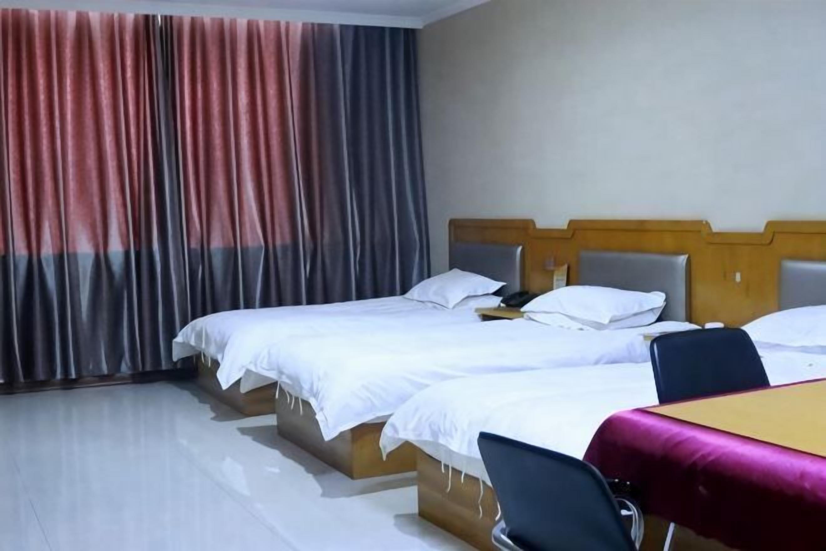 Ein Hotelzimmer mit drei Betten, einem Holzkopfende, einem Tisch mit Tischdecke und einem Stuhl.