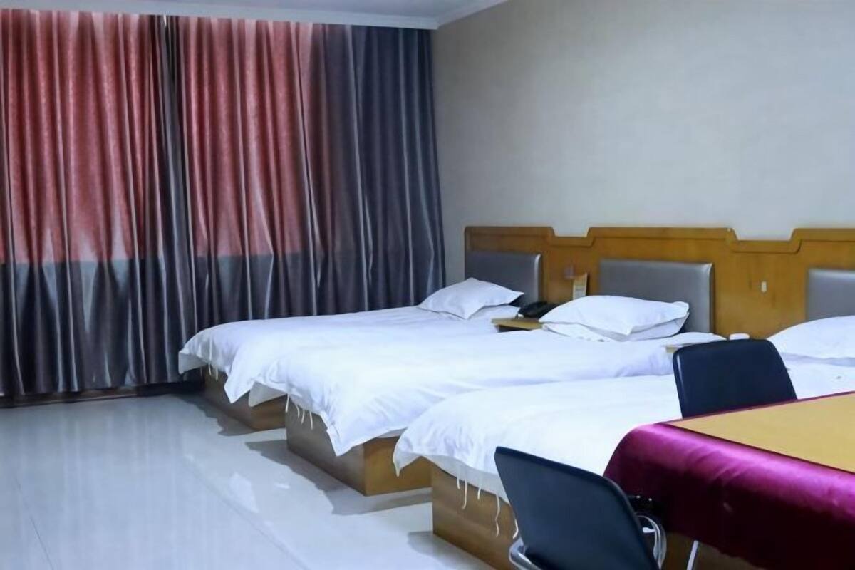 Camera d'albergo con tre letti, una testiera in legno, un tavolo con tovaglia e una sedia.