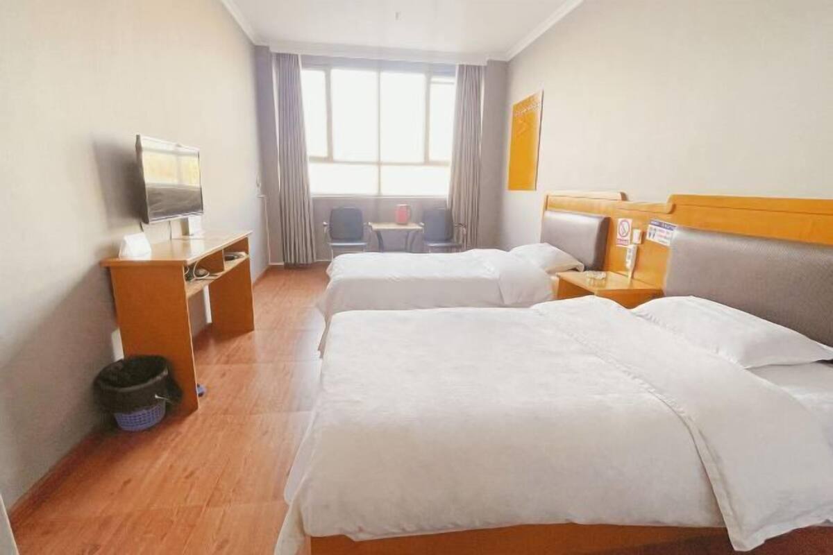 Una camera d'albergo con due letti, una scrivania, una televisione e una finestra con tende.