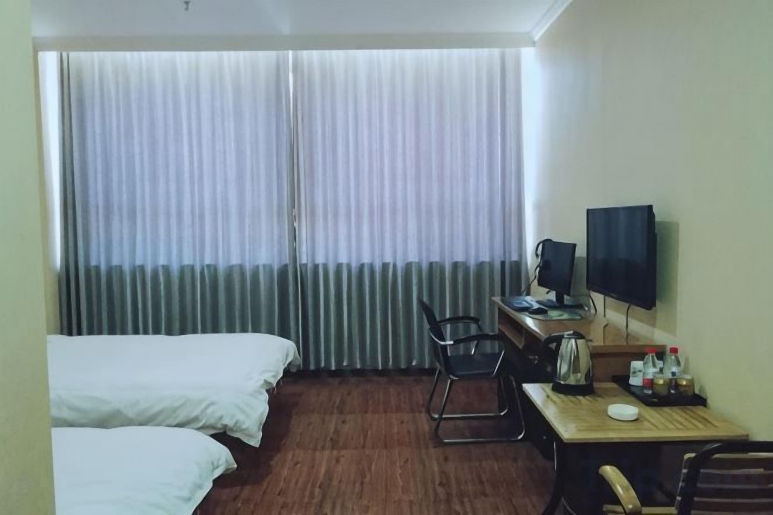 A hotel room with two beds, a desk with a computer, a chair, and a television on the wall.