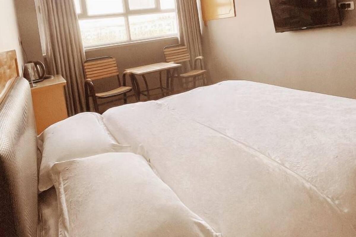 Una camera d'albergo con un letto grande, un tavolino, due sedie e una finestra con tende.