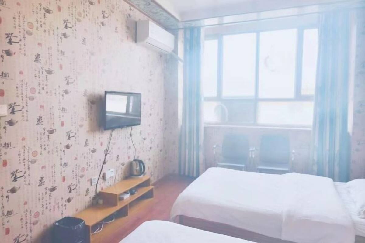 Camera d'albergo con due letti, una televisione, uno scaffale in legno e una finestra con tende.