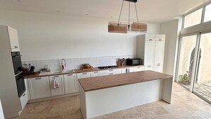 A modern kitchen with a central island, white cabinetry, and a large window providing natural light. - Charming house (Travaillan)